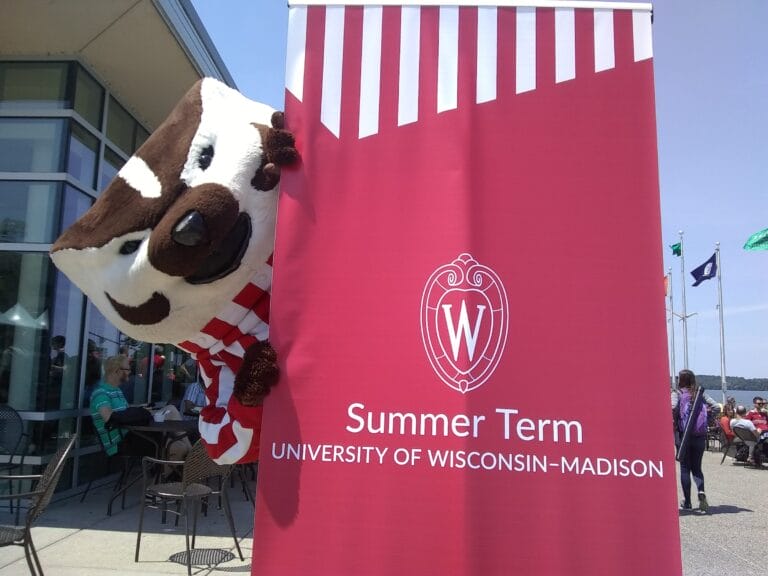 Bucky Badger peeking from behind a red Summer Term banner