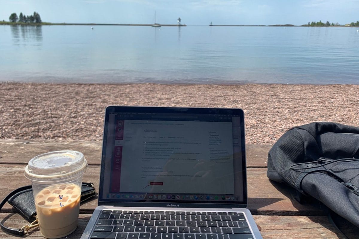 Laptop and iced coffee on rocky beach with lake view in background