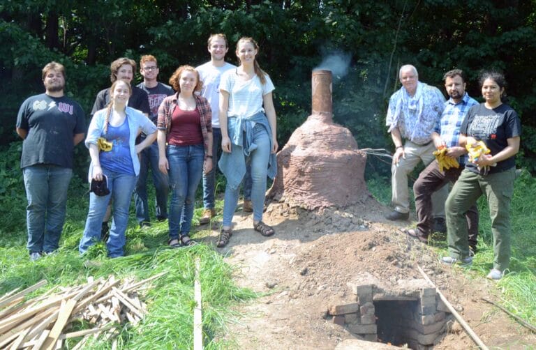 students and professor standing outside around an outdoor kiln