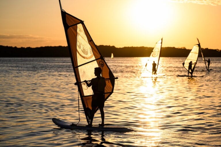 Silhouette of three silhouettes sailing on the lake at sunset