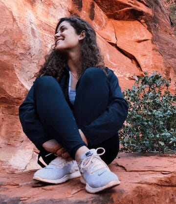 Marie Tuchscherer sits cross-legged on rocks of red cliff