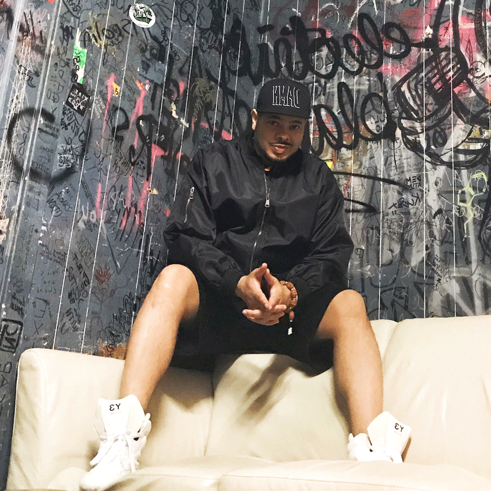 Hip hop promoter Dana Burton sits on a couch with a graffiti splattered wall in the background