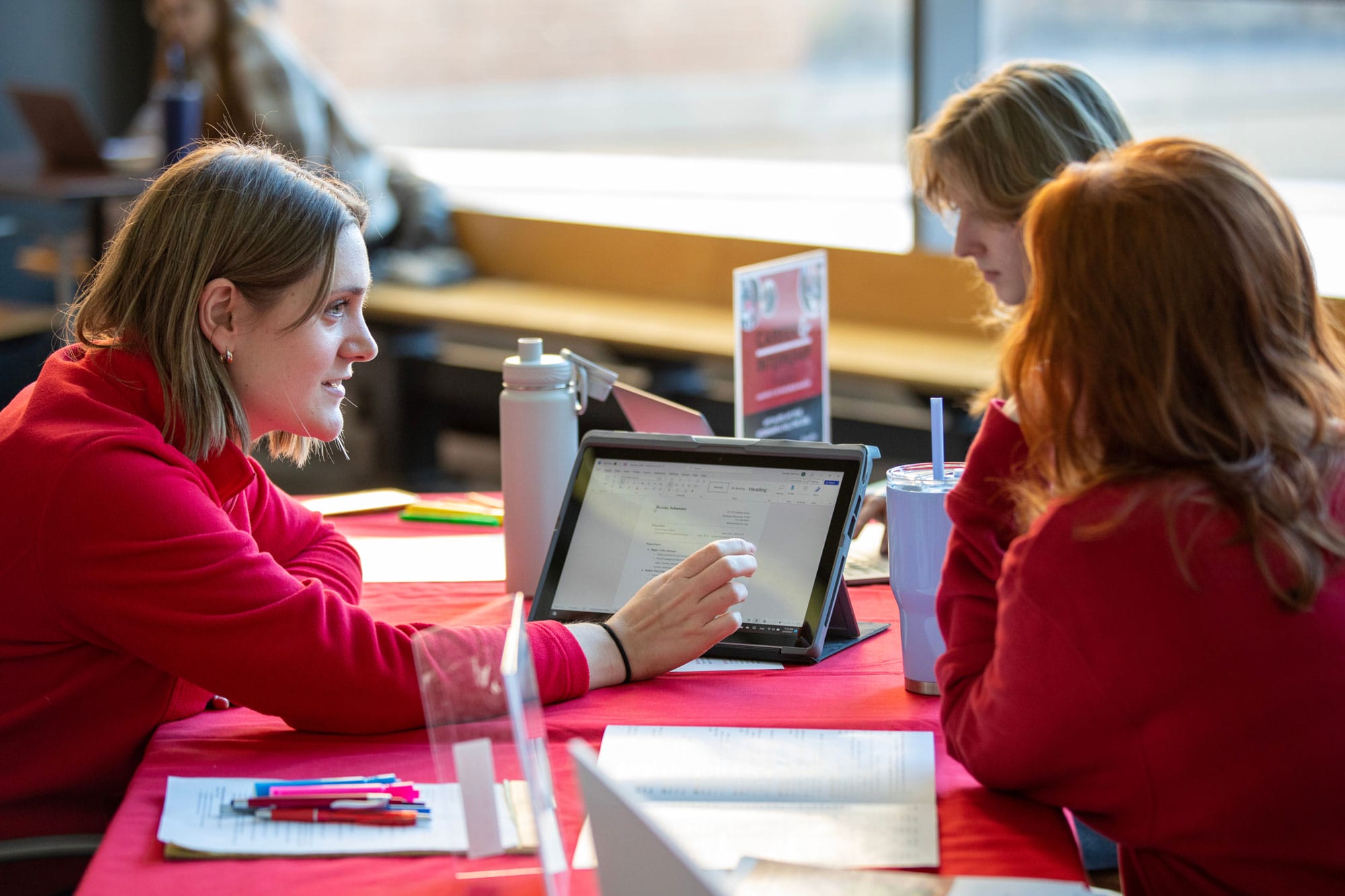 A career advisor and two students review a résumé on a tablet at a study table.