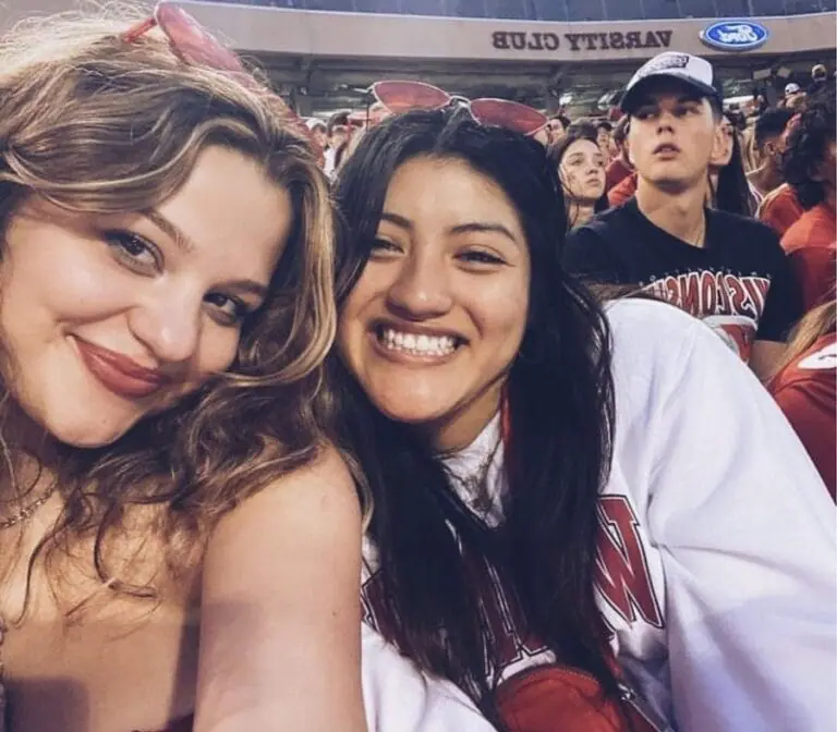 Two UW students huddle in close to each other smiling in the crowd at a UW Badger football game in Camp Randall Stadium