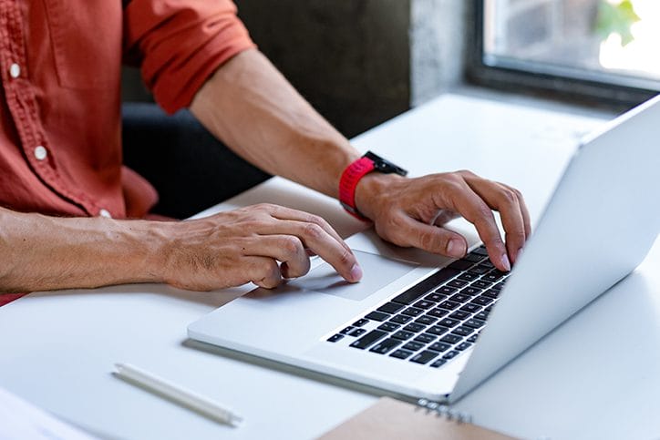 Hands of an unrecognisable man typing on his laptop.