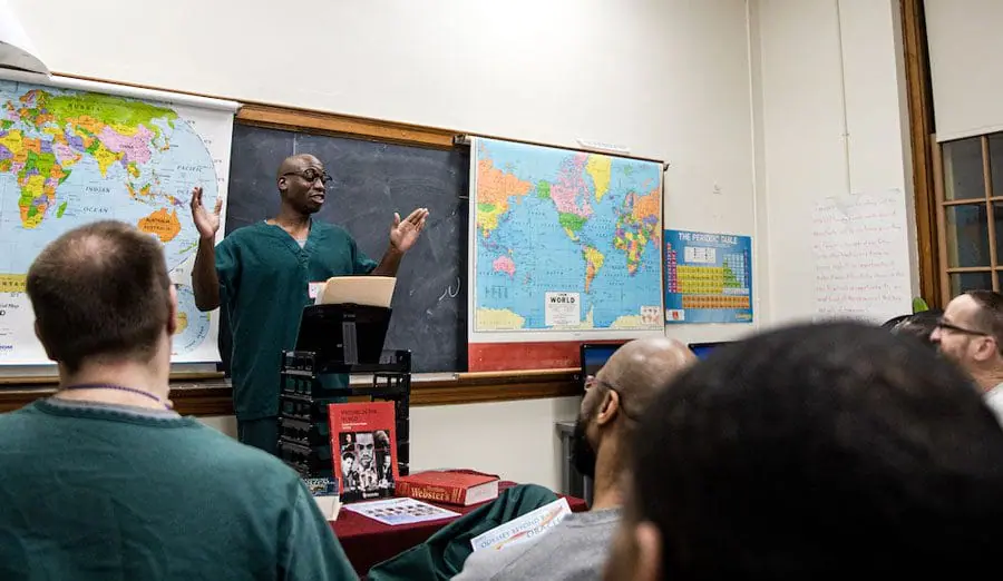 Men gathered in a classroom in a correctional facility listen to a fellow classmate who talks behind a podium.