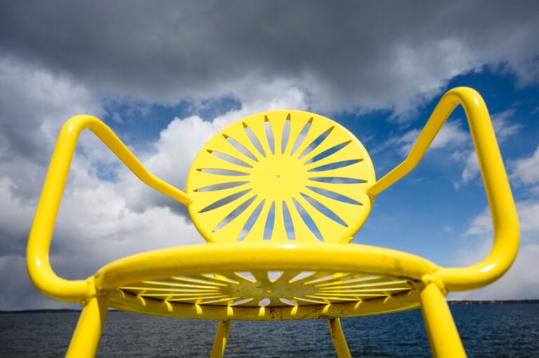 Close up of a yellow terrace chair behind a cloudy sky.