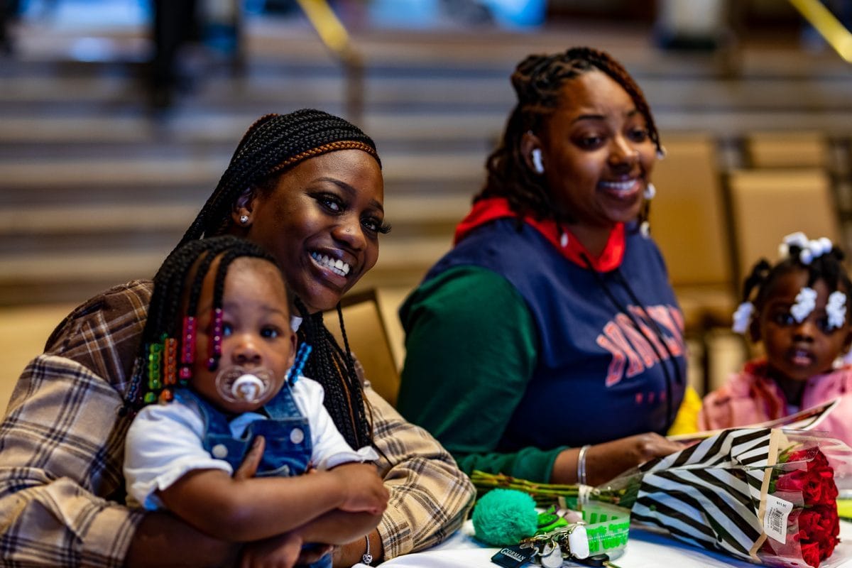 Odyssey Project 2022 graduate smiles while seated at the table with family. She is holding her young daughter on her lap.