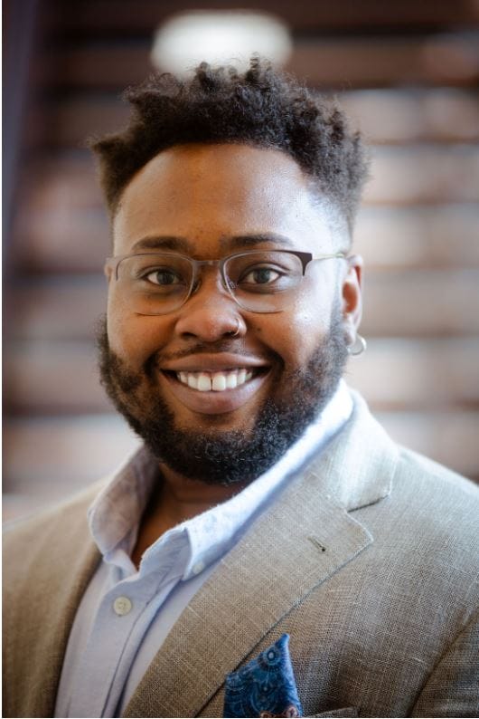 headshot of Ace Hilliard, smiling with glasses on