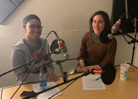 Jen and Takeyla sitting at table with mics in radio station