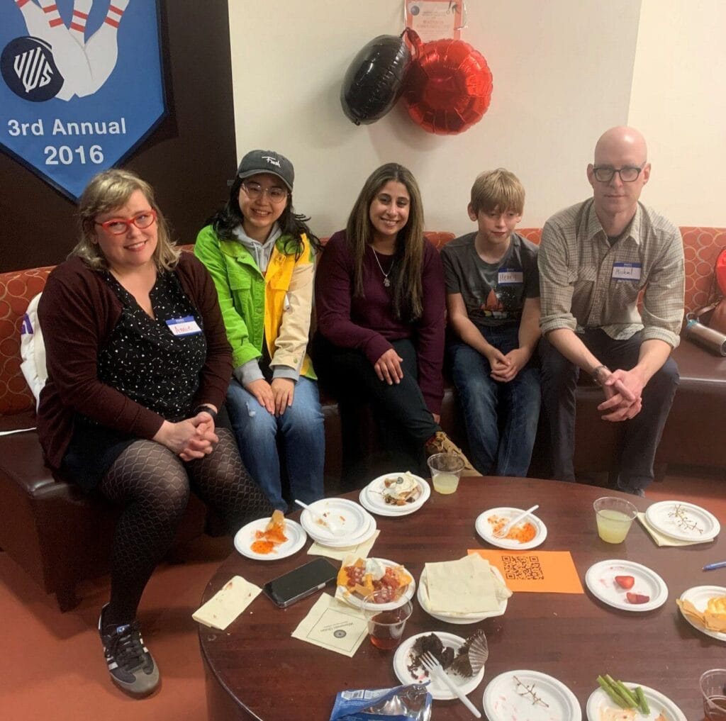 group of students and family sitting behind a table, smiling