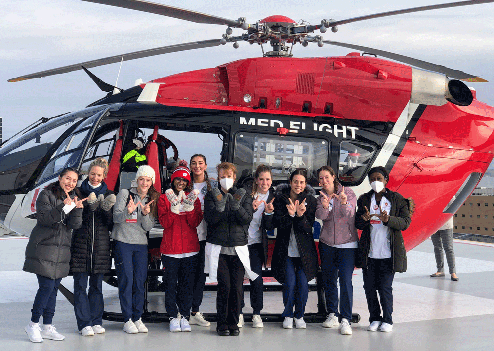 Christine Fifarek and fellow medical students standing in front of a medflight helicopter, sharing the Wisconsin "W"