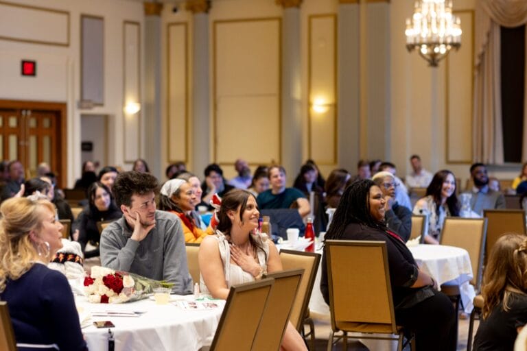 A seated crowd watches an unseen student speaker at awards reception