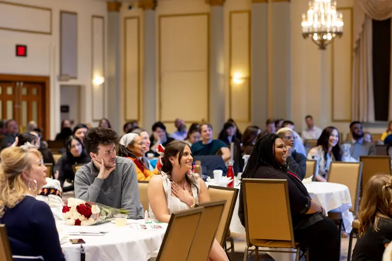 A seated crowd watches an unseen student speaker at awards reception