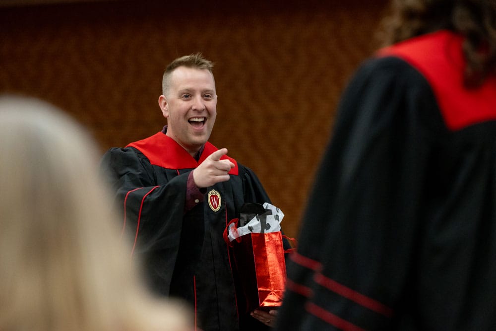 John in his graduation gown pointing to a fellow student