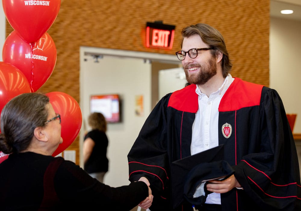 Troy wearing his graduation gown shaking Leanne's hand