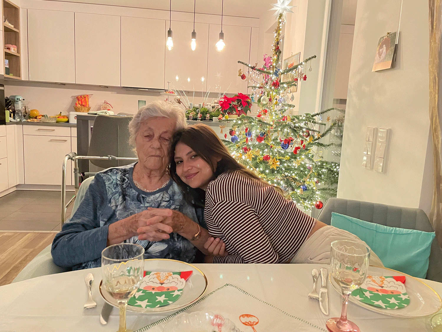 Cindy and her grandmother sitting at a kitchen table, smiling in front of a christmas tree