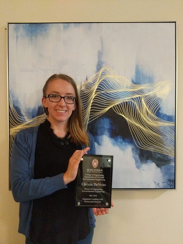 Christa DeVries holds a plaque in front of framed artwork.