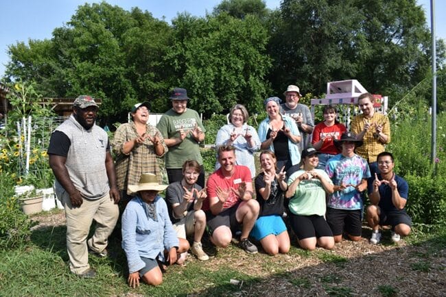 Students and staff sitting and standing in a garden, some giving the "W" for Wisconsin