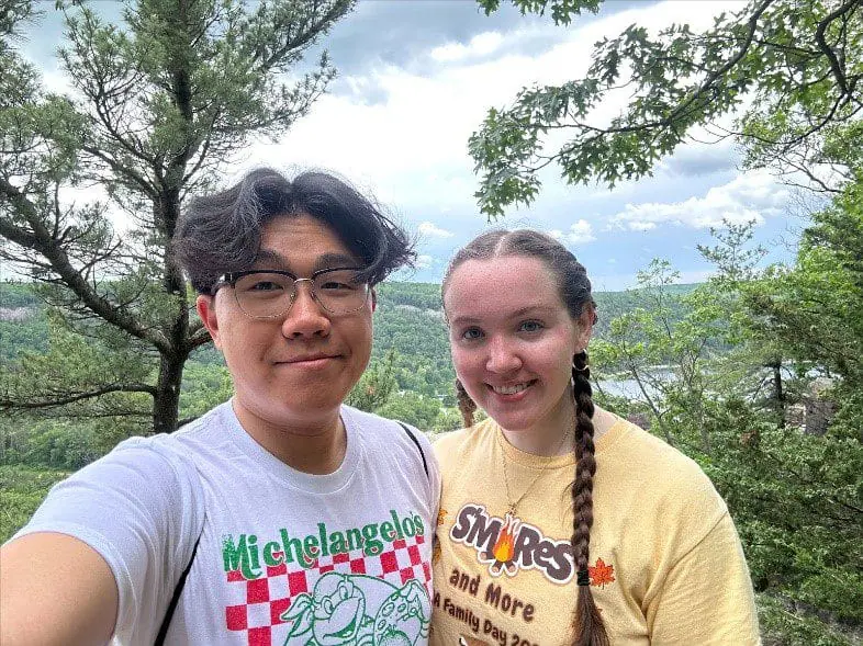 Two people standing in front of green trees and a blue sky, smiling