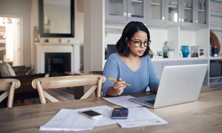 A woman using a laptop studying at a kitchen table