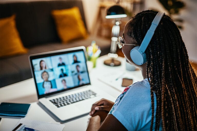 A student wearing headphones looks at her laptop during a video chat.