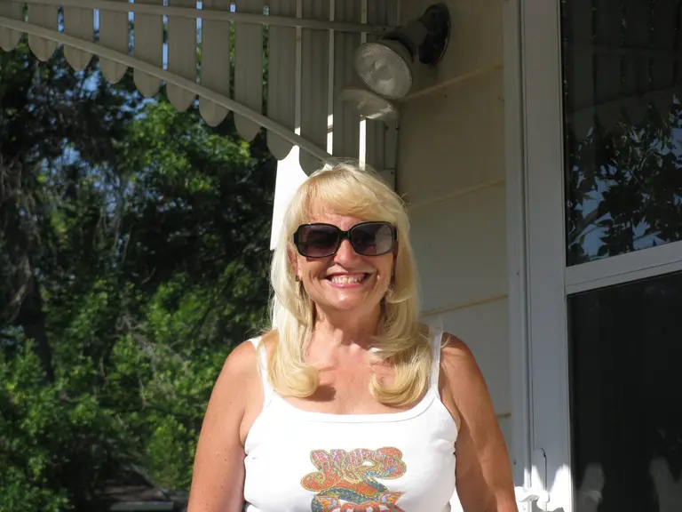 Jeannette Eichholz stands in a tank top and sunglasses on her front porch on a sunny day