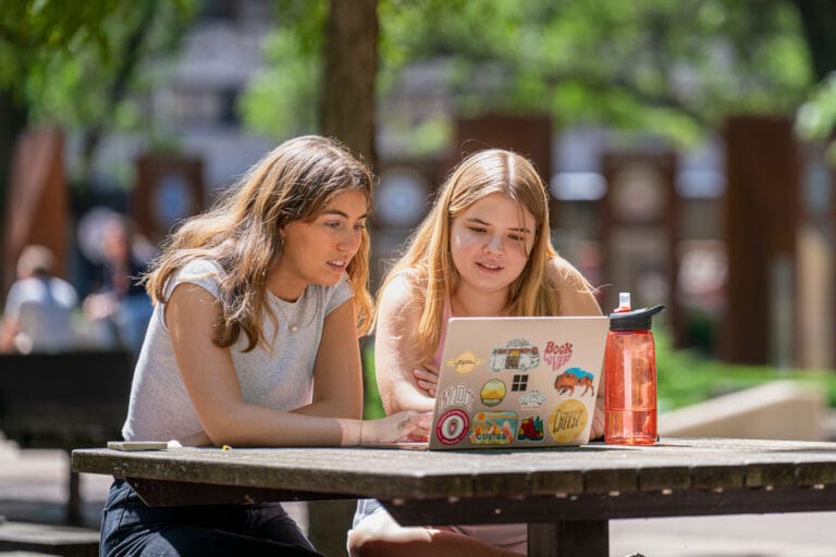 Two UW-Madison students outside, scrolling on their laptop