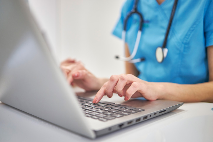 Close-up hands of unrecognizable female physician in medical uniform working typing on laptop keyboard sitting at desk