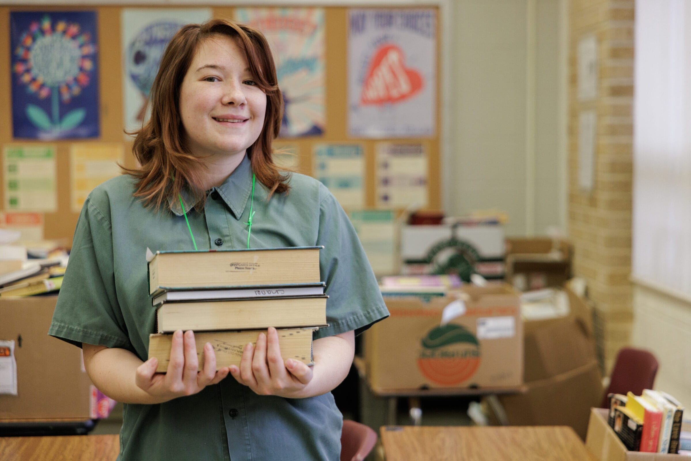 An incarcerated student posing for a picture with a stack of books in her arms