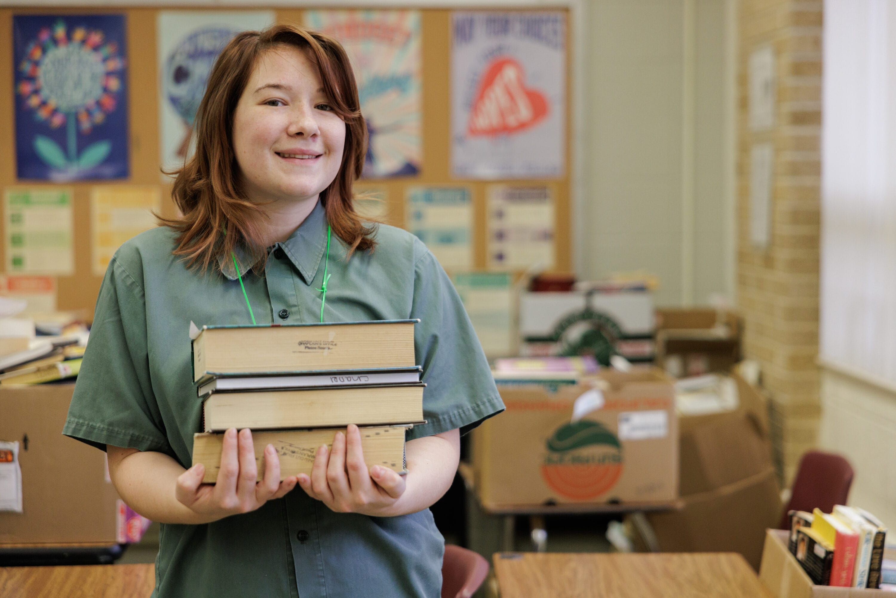 An incarcerated student posing for a picture with a stack of books in her arms