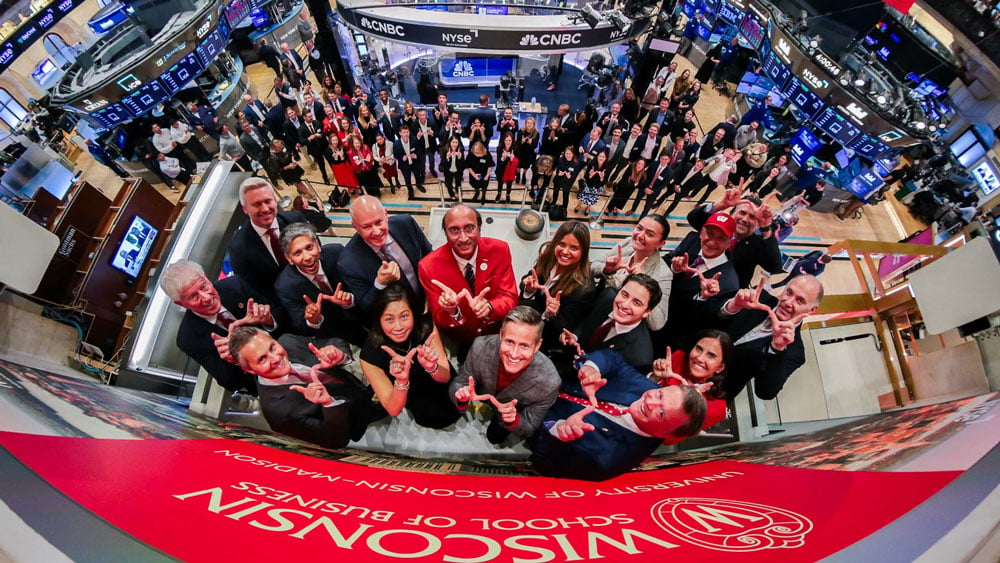 A camera perched atop the bell podium captures the entire Business Badger cohort displaying the “W.” 