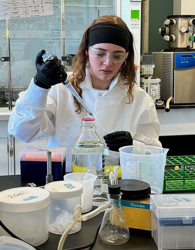 Isadora Collins stands at a counter and works with lab equipment