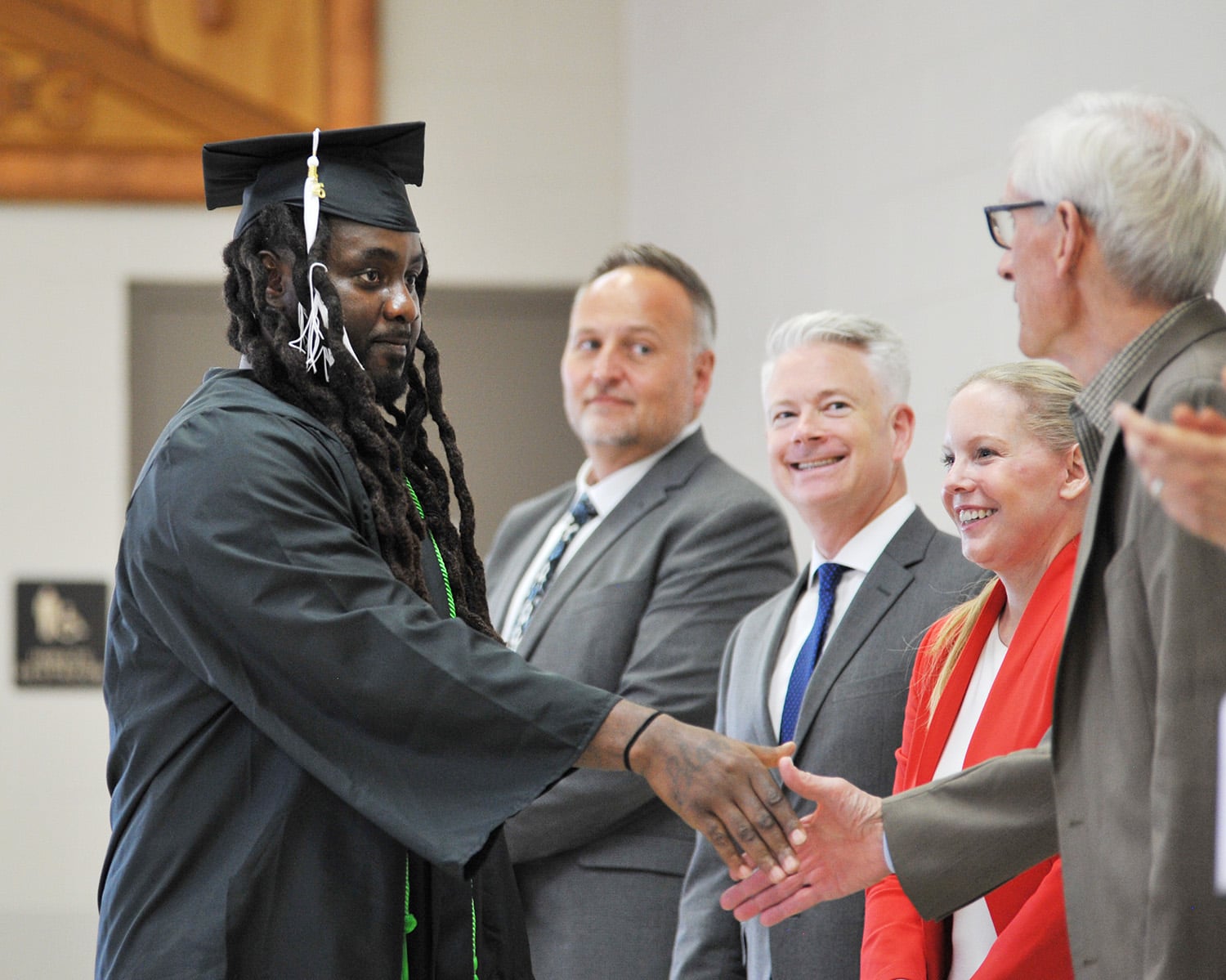 Graduate Michael Allison in his graduation robe shaking Governor Evers's hand
