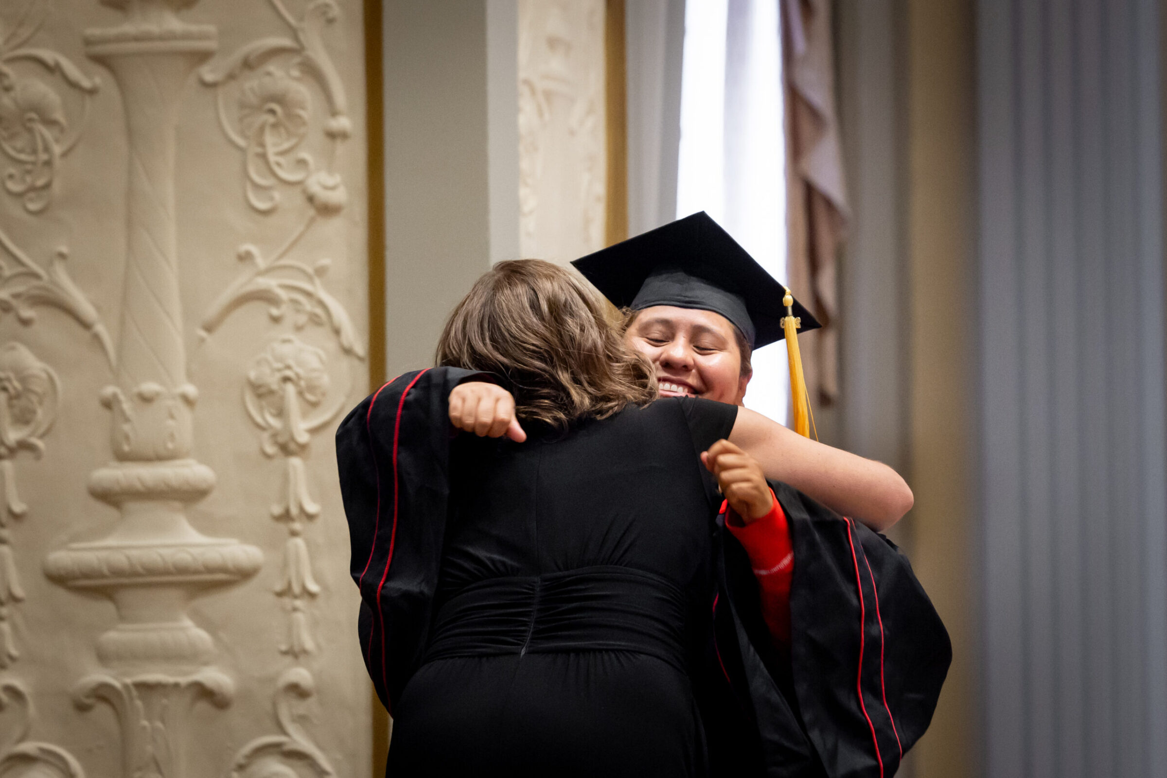 Adult student dressed in cap and gown hugging a staff member of the Division of Continuing Studies.