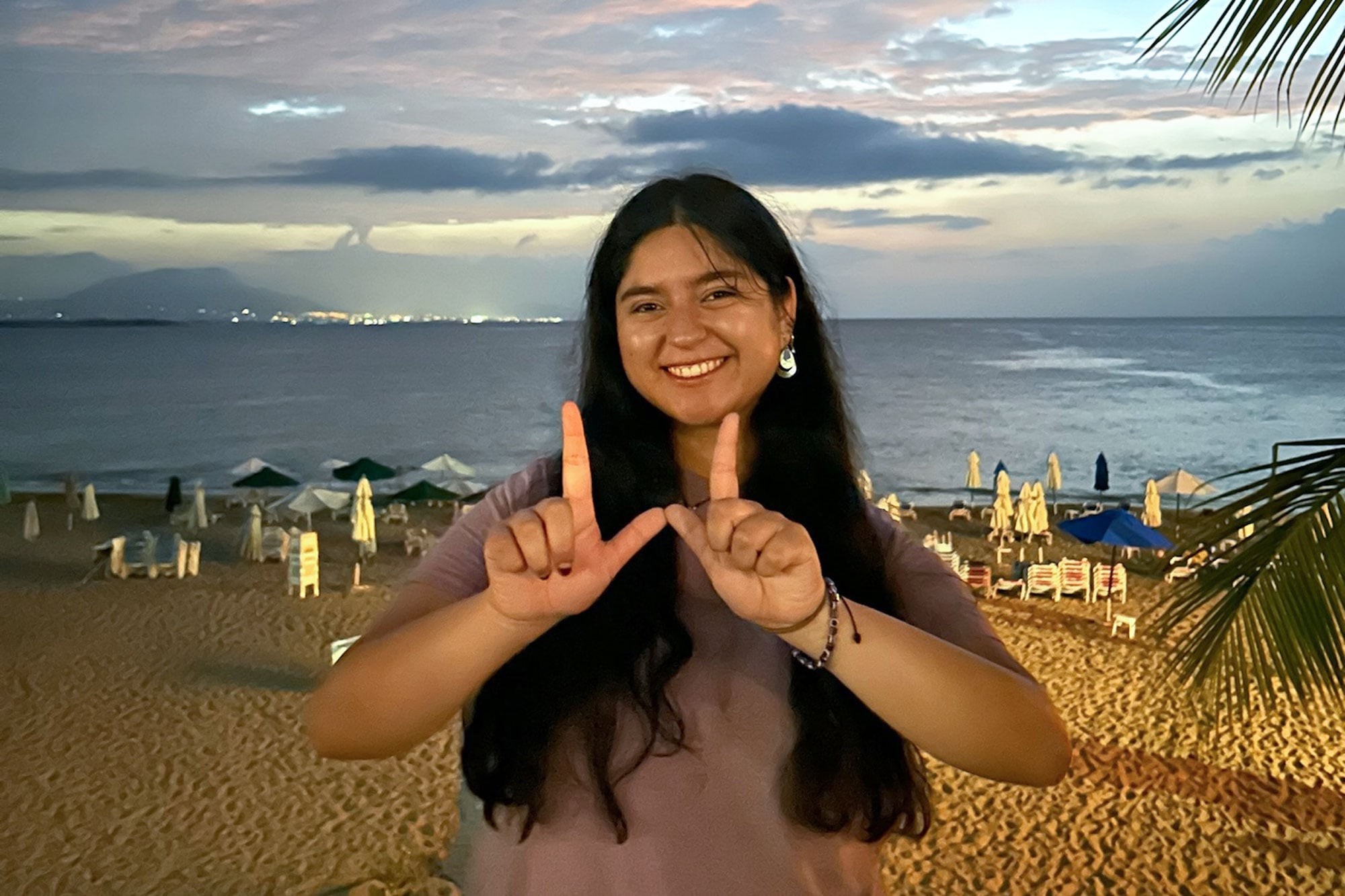 Jimeno Rico-Sotelo stands on the beach and holds up her fingers in the “W” sign.