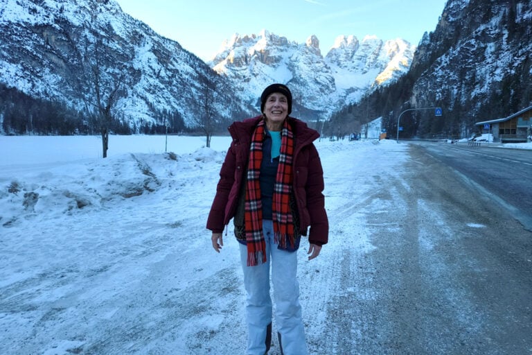 Woman in snow gear standing and smiling, surrounded by snowy mountains.
