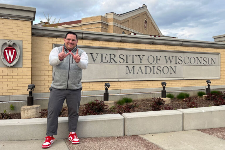 Bobby Adamo throws the "W" hand gesture before an engraved University of Wisconsin-Madison wall.