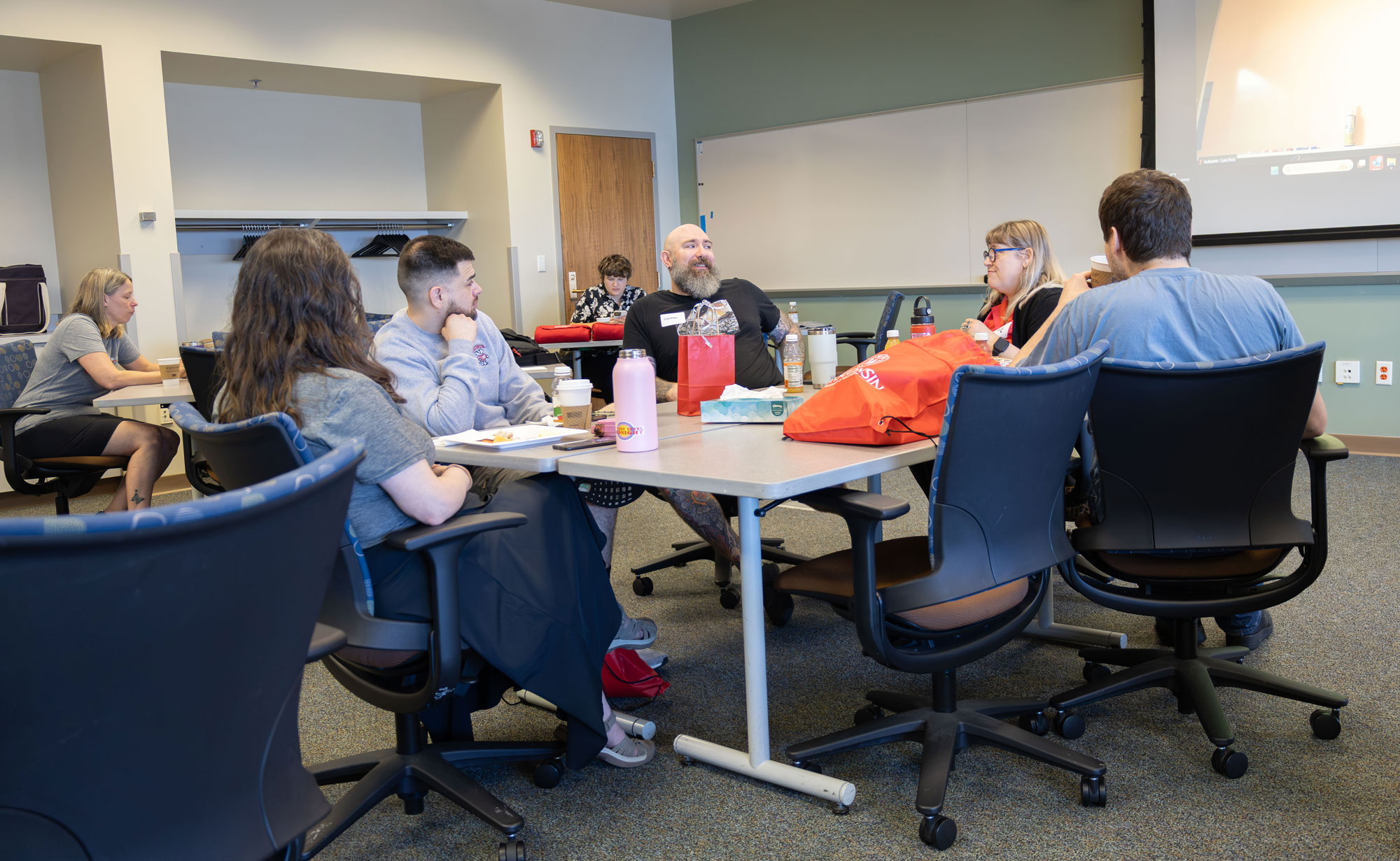 Group of people sitting around a table in a classroom, some talking and some looking at the table.