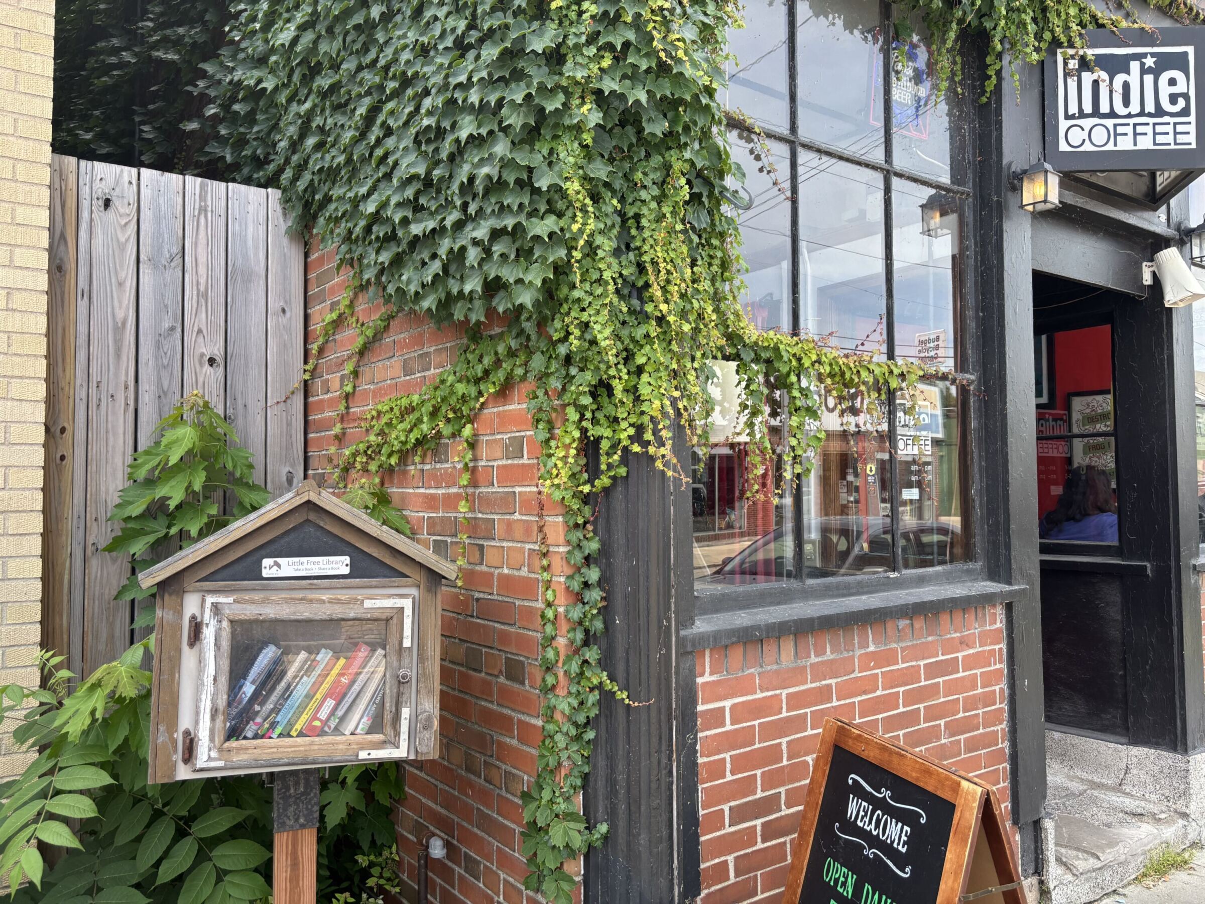 Little Free Library next to Indie Coffee shop with ivy-covered brick wall.
